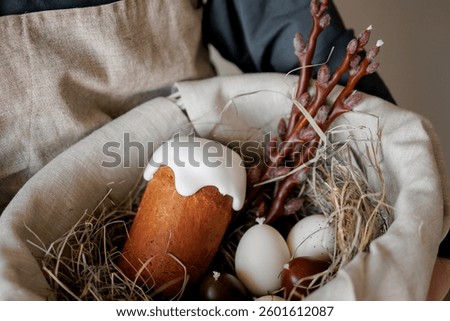 Homemade easter bread in hands on background of natural dyed eggs and spring blossom. Happy Easter! Woman holding baked stylish easter cake with glaze 