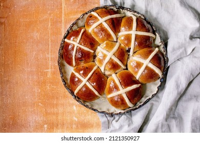 Homemade Easter traditional hot cross buns on ceramic dish over orange stone background with grey linen cloth. Flat lay, copy space