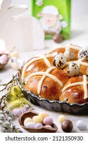 Homemade Easter traditional hot cross buns in ceramic dish with blossom flowers, chocolate candy and quail eggs on white marble table. Easter holiday baking and treats. Close up