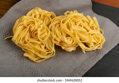 Homemade egg pasta tagliatelle. Macro shot of raw nest noodles, uncooked ribbon fettuccine, dry long rolled macaroni closeup