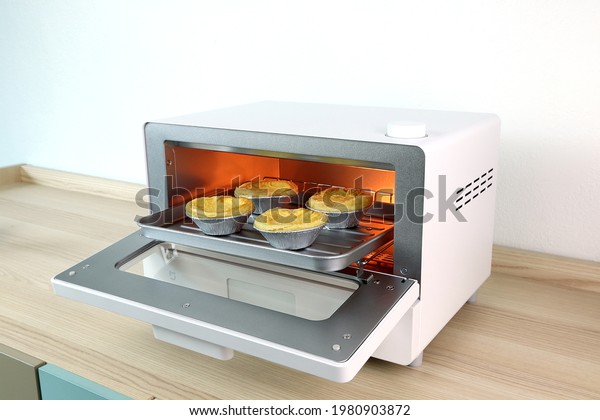 homemade egg tarts are in the white modern\
design toaster oven , countertop or convection oven on the wooden\
table with white cement wall background in minimal design kitchen\
for making the\
breakfast