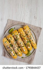 Homemade Elote Mexican Street Corn on a plate on a white wooden surface, top view. Flat lay, overhead, from above. Copy space.