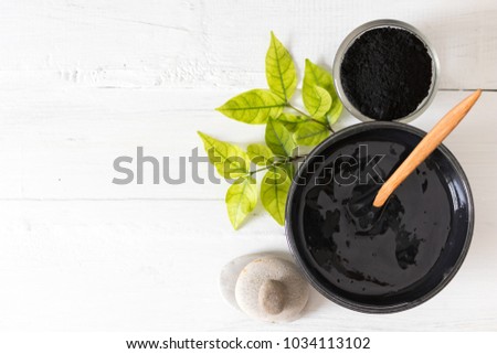 Homemade facial mask and scrub by activated charcoal powder and yogurt on white wooden background