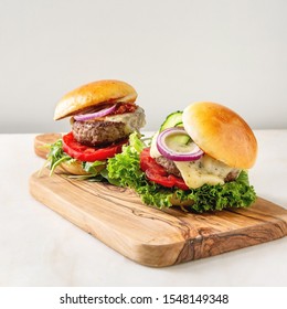 Homemade Fast Food Burger Classic Hamburger Or Cheeseburger With Beef, Salad, Cheese And Tomato Served On Ceramic Plate On White Marble Kitchen Table. Copy Space.