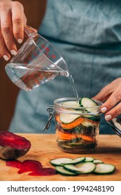 Homemade fermented vegetables. Woman pouring water in the jar with vegetables. 