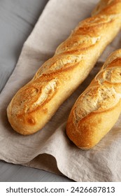 Baguette de pan francés casero sobre un fondo gris, vista lateral.