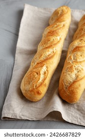 Baguette de pan francés casero sobre un fondo gris, vista lateral.