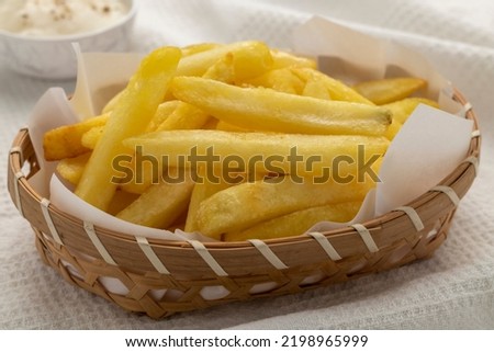 Homemade French fries, finger chips or French-fried potatoes served in a flat bamboo basket lined with white paper together with a cup of sour cream. 