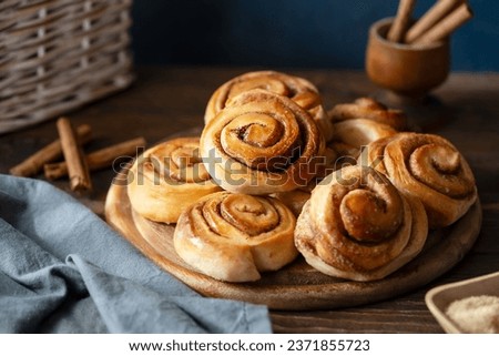 Homemade fresh baked cinnamon rolls on a wooden board with cinnamon sticks, sugar and napkin Wooden and dark background