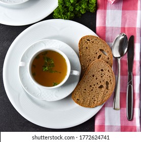 Homemade Fresh Cooked Beef Broth Served In A White Soup With Sourdough Bread On A Table. Closeup And Overhead View