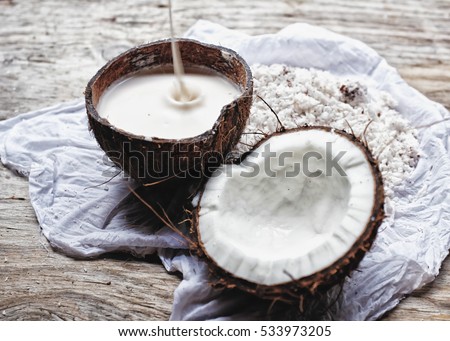 Homemade fresh hand traditional hand pressed coconut milk in a coconut bowl with slight drop of coconut milk and a half of coconut. Healthy ingredients. Wooden background/ white linen table cloth. 