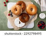 Homemade freshly baked bagels on a parchment paper ready to eat, cinnamon raisin, sesame and plain bagel served with cream cheese and fresh berries