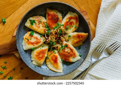 Homemade fried Polish potato pierogi with fried onion top view on a cermaic dark plate 