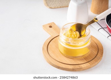 Homemade ghee butter in small glass jar on white kitchen table background, copy space. Melted organic ghee clarified butter, Bio Ayurveda Lactose free high quality animal fat source