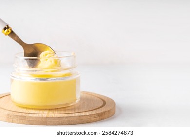 Homemade ghee butter in small glass jar on white kitchen table background, copy space. Melted organic ghee clarified butter, Bio Ayurveda Lactose free high quality animal fat source