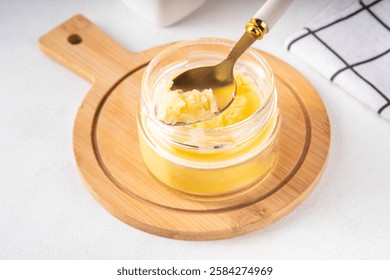 Homemade ghee butter in small glass jar on white kitchen table background, copy space. Melted organic ghee clarified butter, Bio Ayurveda Lactose free high quality animal fat source