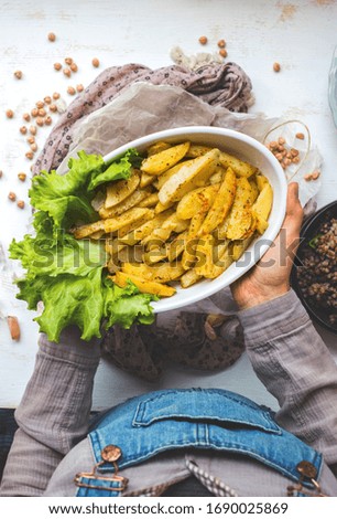Homemade golden salty french fried potato with green salad leaves. Roasted or grilled spicy potato sticks in woman hands.