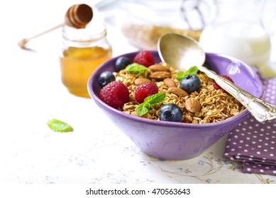 Homemade granola with fresh berry for a breakfast in a purple bowl on a light background.