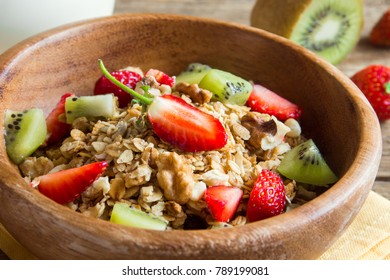 Homemade granola with fresh fruits (strawberry and kiwi) and nuts in wooden bowl for healthy diet breakfast close up