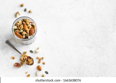 Homemade granola with nuts and seeds in glass jar. Organic granola for healthy breakfast on white, top view, copy space.