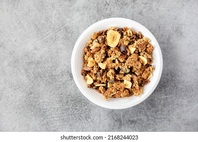 Homemade granola in a white bowl on a white background, overhead view. Homemade whole grain musli with bananas and dark chocolate for breakfast. Top view, light, airy, clean. Breakfast cereal.