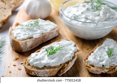 Homemade greek tzatziki sauce in a glass bowl with sliced bread on a wooden board. Close-up, horizontal image, selective focus on bread - Powered by Shutterstock