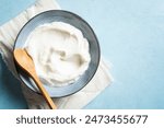 Homemade Greek Yogurt in bowl on blue background, top view, copy space. Organic plain greek yogurt, labneh cream cheese, sour cream for healthy breakfast.