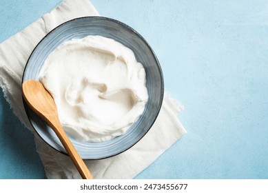 Homemade Greek Yogurt in bowl on blue background, top view, copy space. Organic plain greek yogurt, labneh cream cheese, sour cream for healthy breakfast.