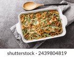 Homemade Green Bean Casserole with crispy fried onions on the baking dish on the table. Horizontal top view from above
