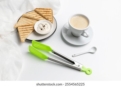 Homemade grilled toasts for breakfast with cheese sauce, a white porcelain cup of black coffee, a stainless steel salad tongs and a spoon on the white background. Top view. - Powered by Shutterstock