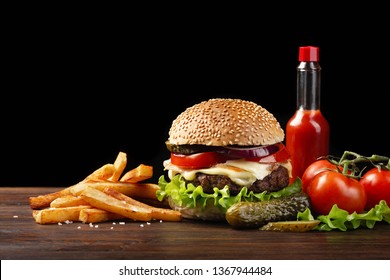 Homemade hamburger close-up with beef, tomato, lettuce, cheese, onion, french fries and sauce bottleon wooden table. Fastfood on dark background. - Powered by Shutterstock