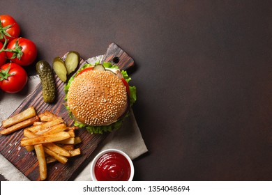 Homemade Hamburger With Ingredients Beef, Tomatos, Lettuce, Cheese, Onion, Cucumbers And French Fries On Cutting Board And Rusty Background. Top View With Place For Your Text.