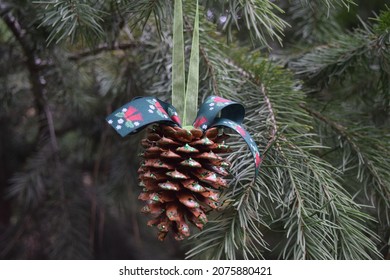Homemade hanging pinecone with bells ribbon and green glitter.