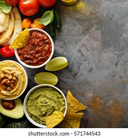 Homemade Hummus, Salsa And Guacamole With Corn Chips And Vegetables Overhead View