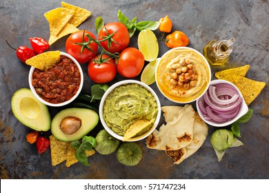 Homemade Hummus, Salsa And Guacamole With Corn Chips And Vegetables Overhead View