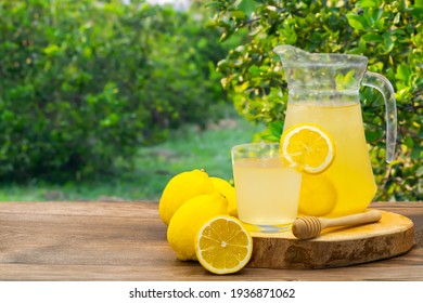 Homemade Ice Honey Lemon Soda Organic Probiotic Drink In A Glass With Lime Fruit On Wooden Table With Blur Lemon Tree Farm And Garden Background.