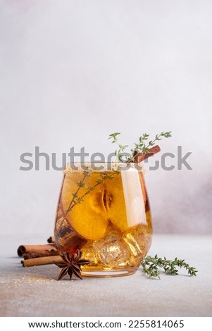Homemade ice sweet apple cider, cocktail or mocktail with cinnamon, thyme and anise in glass for tasty and refreshing break on grey concrete background