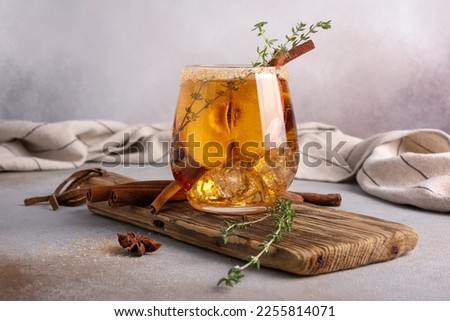 Homemade ice sweet apple cider, cocktail or mocktail with cinnamon, thyme and anise in glass for tasty and refreshing break on grey kitchen background
