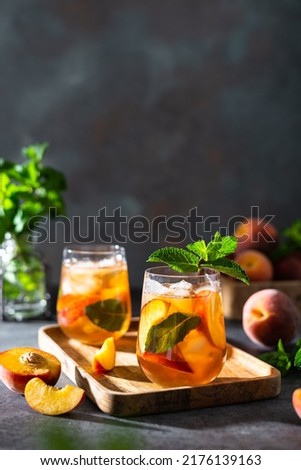 Homemade iced lemonade with ripe peaches and fresh mint. Fresh peach ice tea in glasses on a dark background with ingredients. Summer refreshing beverage recipe. Bar, cafe menu. Copy space for text