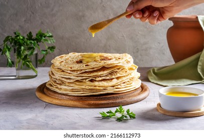 Homemade Indian Chapati or Roti on grey concrete background with human hand pouring butter ghee over 