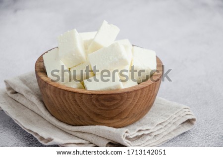 Homemade Indian paneer cheese made from fresh milk and lemon juice, diced in a wooden bowl on a gray stone background. Horizontal orientation. Close up