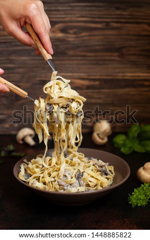 Homemade Italian fettuccine pasta with mushrooms and cream sauce (Fettuccine al Funghi Porcini). Traditional Italian cuisine. Served on a dark table with a rustic wooden background. Close-up. Vertical