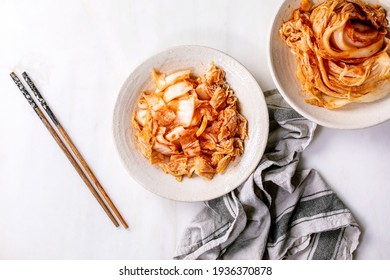 Homemade korean traditional fermented appetizer kimchi cabbage whole and chopped served in ceramic plate with chopsticks over white marble background. Flat lay, space