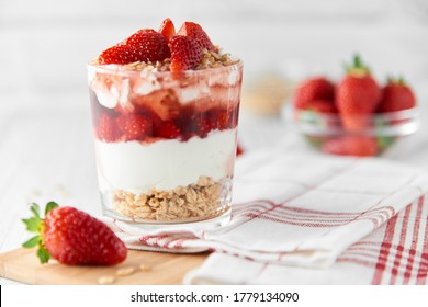 Homemade layered dessert with fresh strawberries, cream cheese or yogurt, granola and strawberry jam in glass on white wood background. Healthy organic breakfast or snack concept. Selective focus. - Shutterstock ID 1779134090