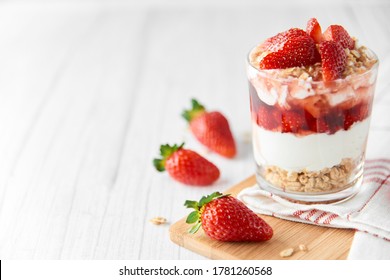 Homemade layered dessert with fresh strawberries, cream cheese or yogurt, granola and strawberry jam in glass on white wood background. Healthy organic breakfast or snack concept. Selective focus. - Shutterstock ID 1781260568