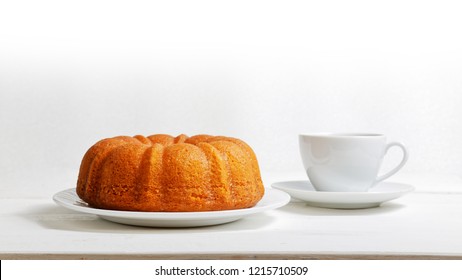 Homemade Lemon Cake In The Form Of A Ring Soaked With Lemon Syrup And Cup Of Tea Or Coffee On White Wooden Table. Front View.