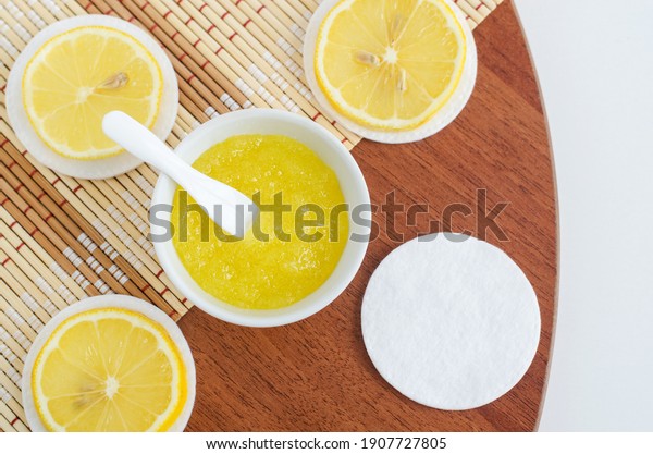 Homemade lemon fruit scrub\
(bath salt, foot soak, facial or hair mask) in a small white bowl\
and cotton pad. Natural beauty treatment and spa recipe. Top view,\
copy space. 
