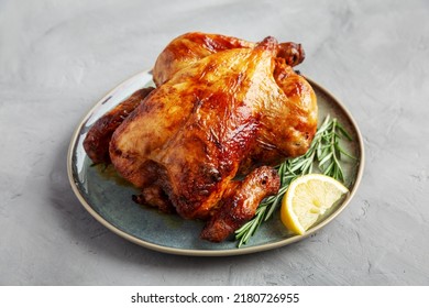 Homemade Lemon and Herb Rotisserie Chicken on a Plate on a gray background, side view. 