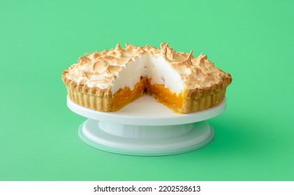 Homemade Lemon Meringue Pie On White Cake Stand On A Green Table. Sliced Meringue Cake, With One Layer Of Lemon Custard.