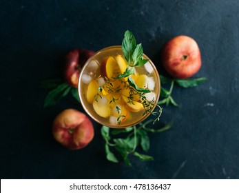 Homemade lemonade drink with fresh sweet peaches, mint leaves and thyme in glass on a dark background